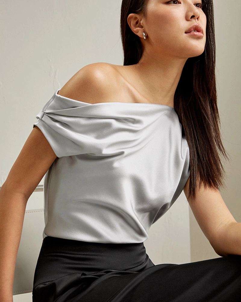 Close-up of fine silk fabric on an off-the-shoulder blouse, highlighting smooth texture and quality stitching.