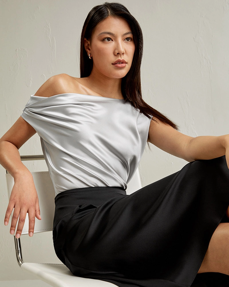 Tailor adjusting measurements on silk off-the-shoulder blouse inside high-end Dongguan clothing workshop.